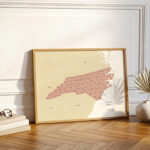 North Carolina map print leaning against a wall beside decorative accents, styled in a warm, contemporary home setting.