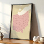 Framed Ohio map leaning on a wooden shelf, surrounded by simple ceramic décor and illuminated by gentle morning light.