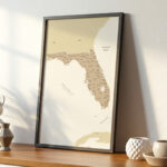 Framed Florida state map leaning on a wooden desk in a bright minimalist room with decorative ceramics.