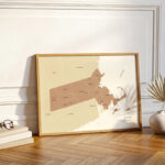 Framed Massachusetts county map leaning against a wall in a bright, modern interior with warm wooden flooring.