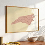 Framed North Carolina counties map hanging above a minimalist console table with warm sunlight casting natural shadows.