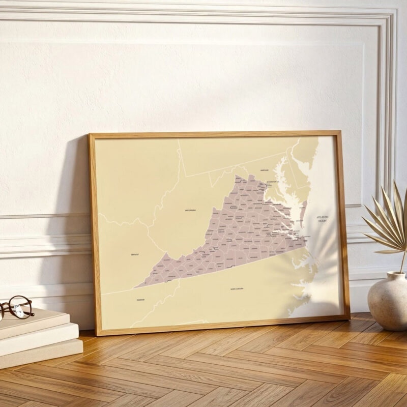 A framed Virginia map positioned on a wooden floor against a decorative wall, illuminated by natural light with soft shadows.