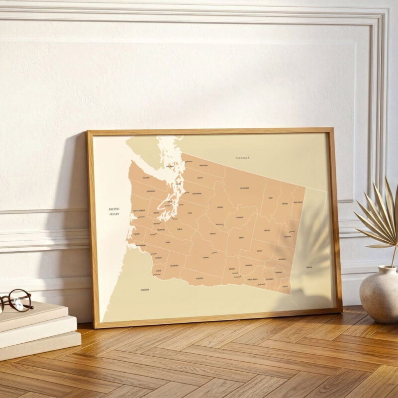 A framed Washington state map resting against a white wall on a wooden floor, styled with warm light and subtle decorative accents